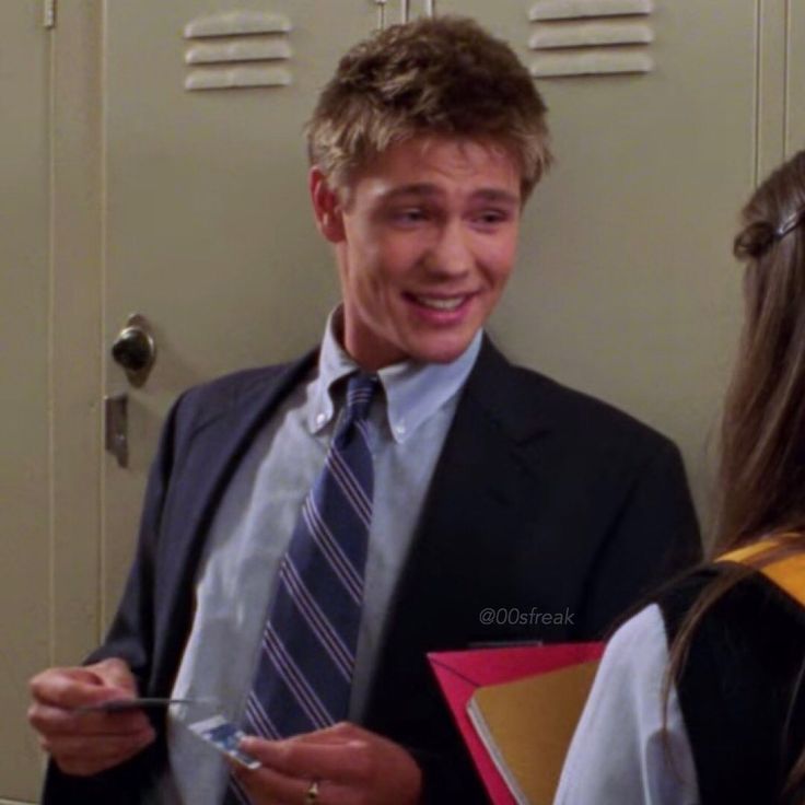 a man in a suit and tie standing next to a woman with folders on her lap