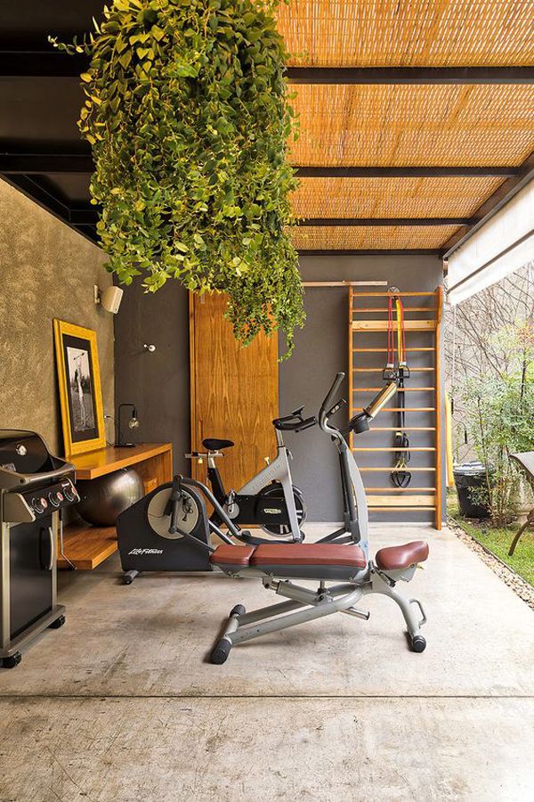 an indoor gym area with exercise equipment and plants hanging from the ceiling, in front of a wood paneled wall