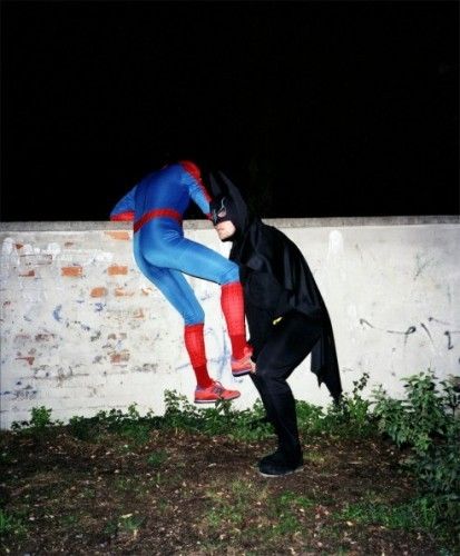 two people dressed up as batman and spider man in front of a white brick wall