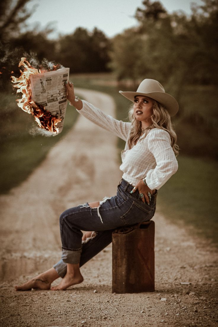 a woman sitting on top of a wooden post holding a newspaper and fire in her hand