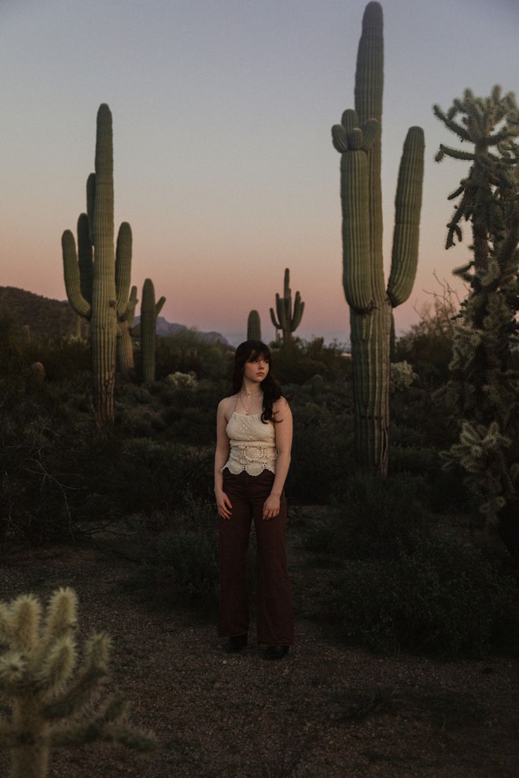 a woman standing in front of some cactus trees at sunset with her hands on her hips