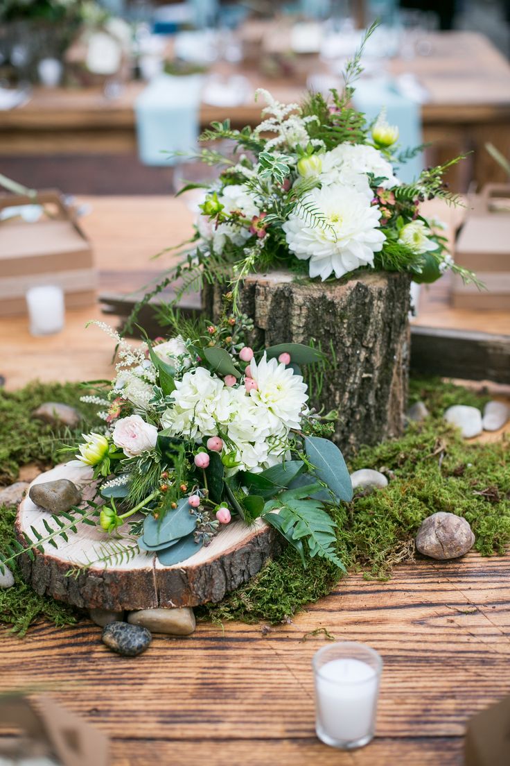 flowers and greenery are placed on top of the wood stumps at this outdoor wedding reception