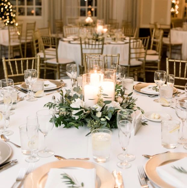 the table is set with white and gold plates, silverware, candles and greenery