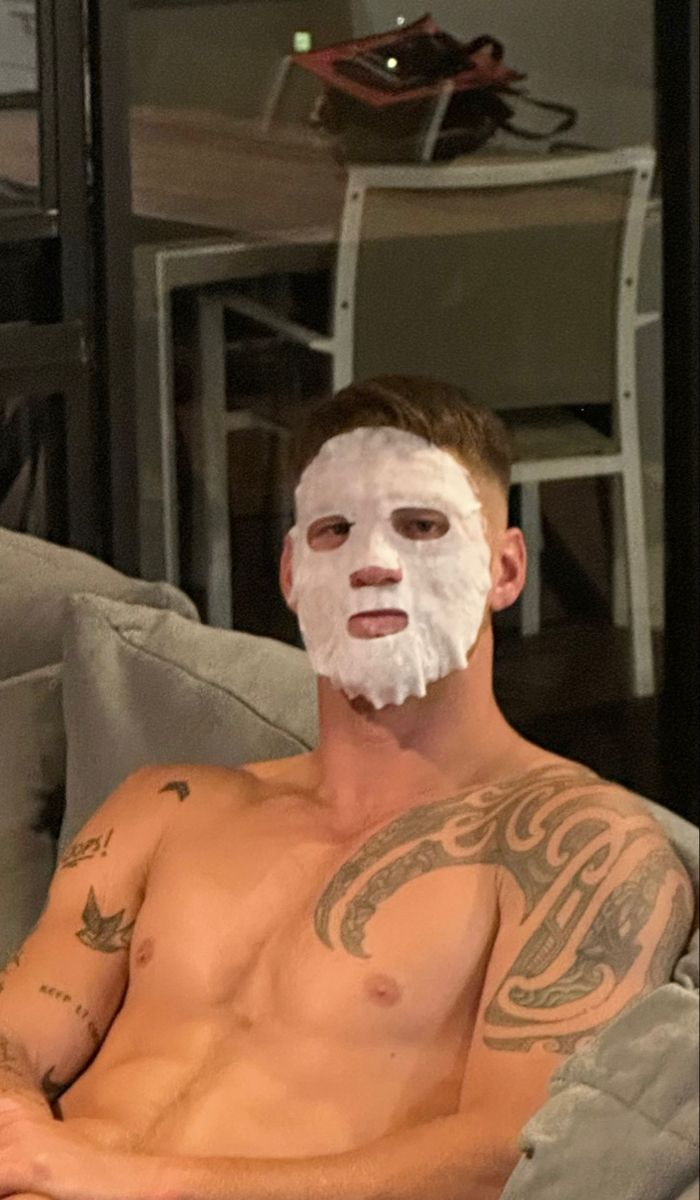 a shirtless man sitting on a couch with a white mask on his face and chest