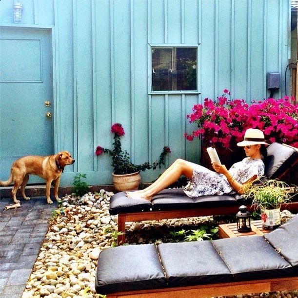 a woman sitting on a chaise lounge in front of a blue building with pink flowers