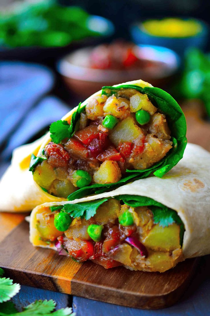 two burritos with meat and vegetables on a cutting board