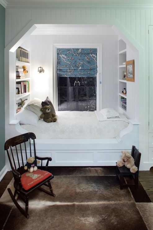 a room with a chair, bookshelf and stuffed animals in the window sill