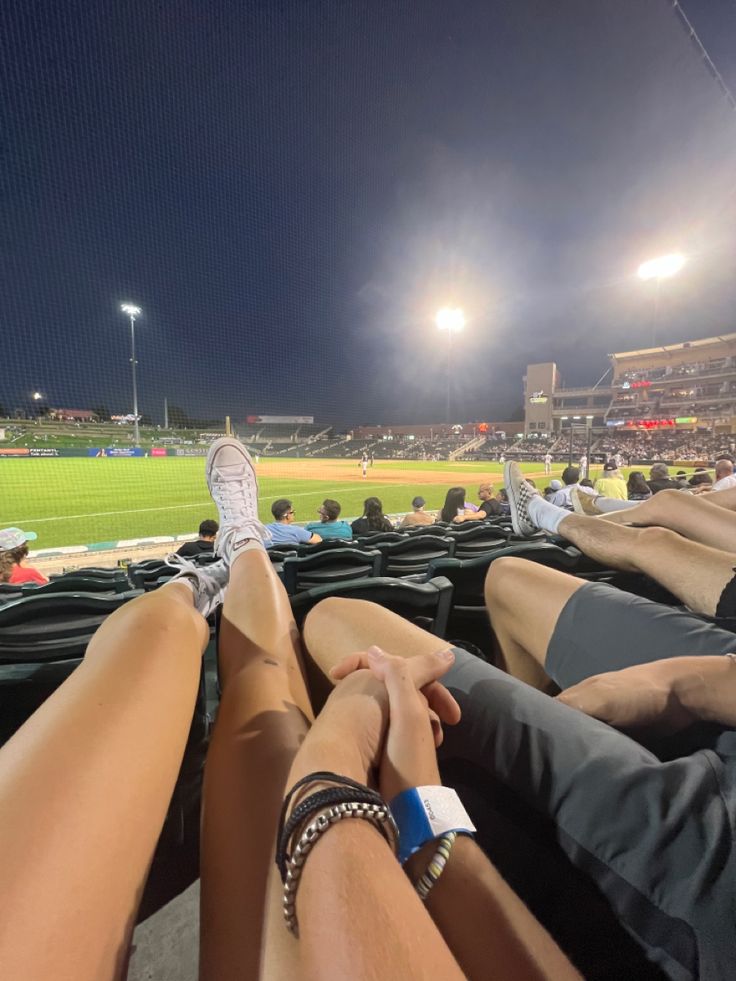 people sitting in the stands at a baseball game with their feet on each other's legs