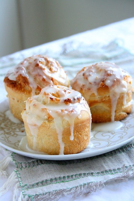 three cinnamon rolls on a plate with icing drizzled over them and sitting on a tablecloth