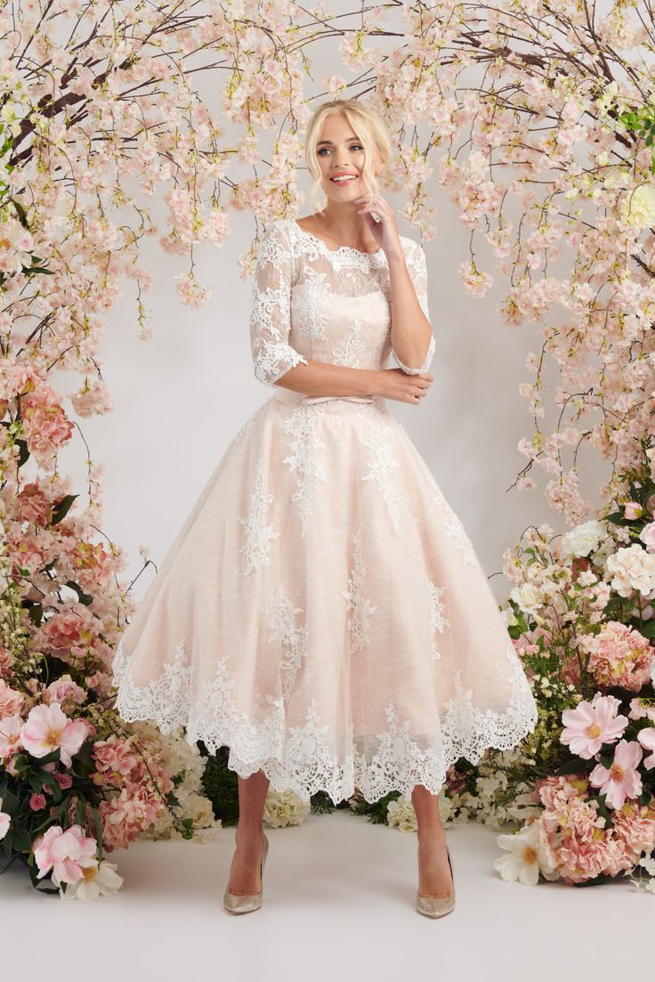 a woman standing in front of a floral arch wearing a dress with white lace on it