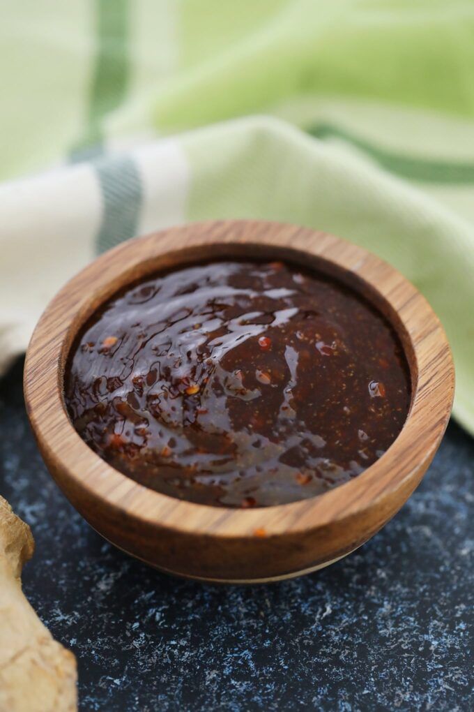 a wooden bowl filled with brown sauce on top of a table next to a piece of bread