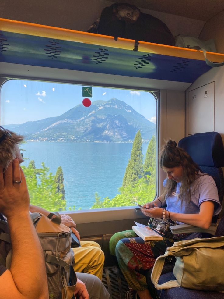 two people are sitting on a train looking out the window at mountains and water in the distance