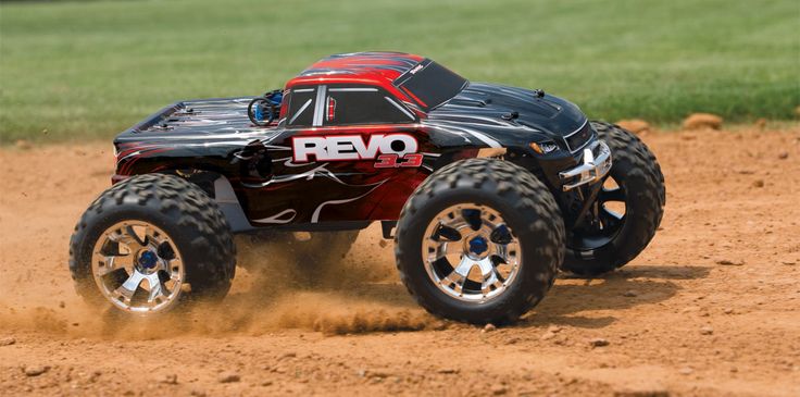 a red and black remote control truck driving on the dirt with grass in the background