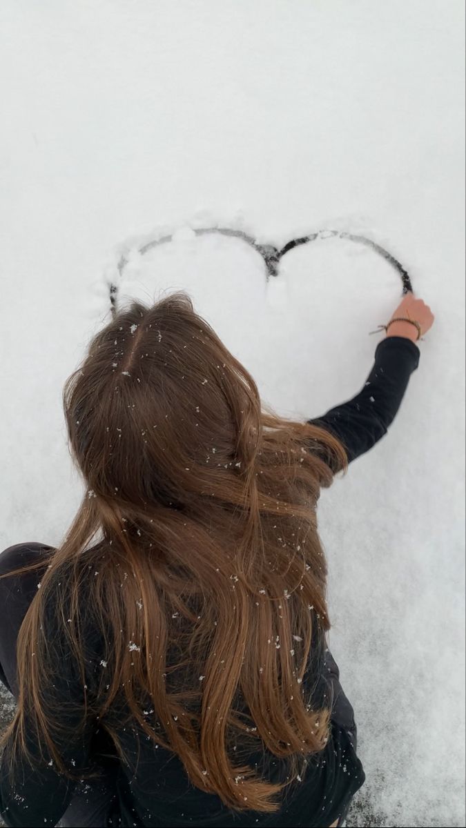 a woman sitting in the snow with her back to the camera holding a heart shaped object