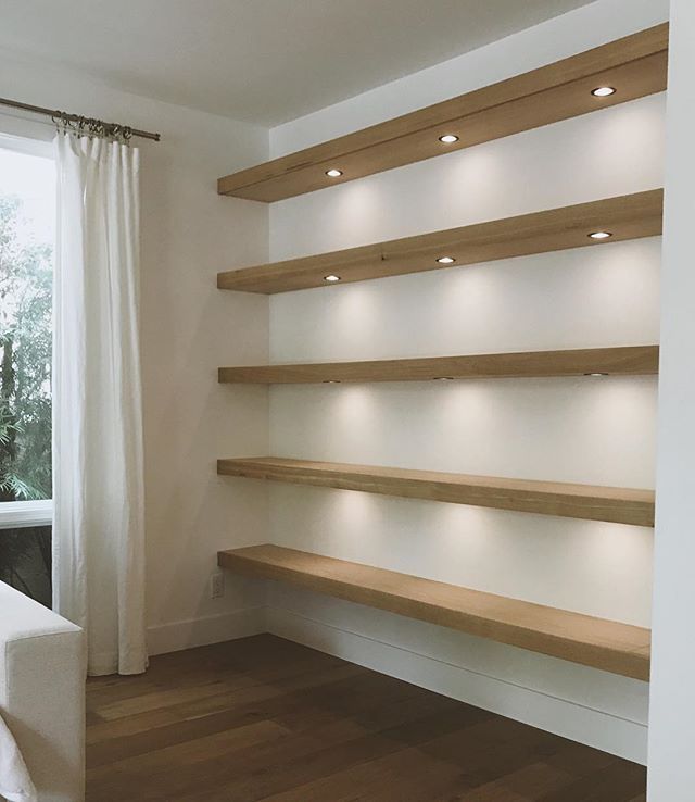 an empty room with white walls and wooden shelves on the wall next to a window