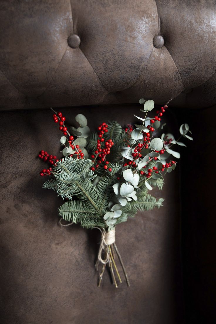 a bouquet of red berries and greenery sits on a brown leather chair with buttons