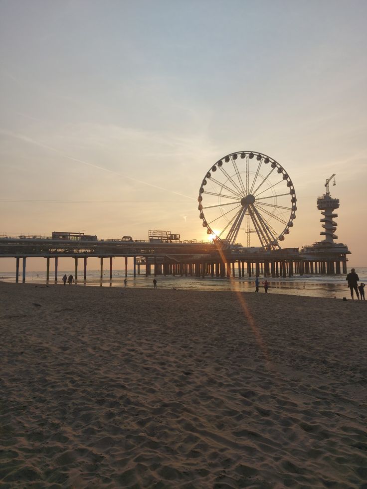 a ferris wheel sitting on top of a sandy beach next to the ocean at sunset