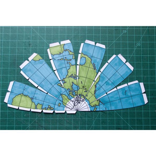 a green cutting mat with blue and white paper cut into the shape of a world map