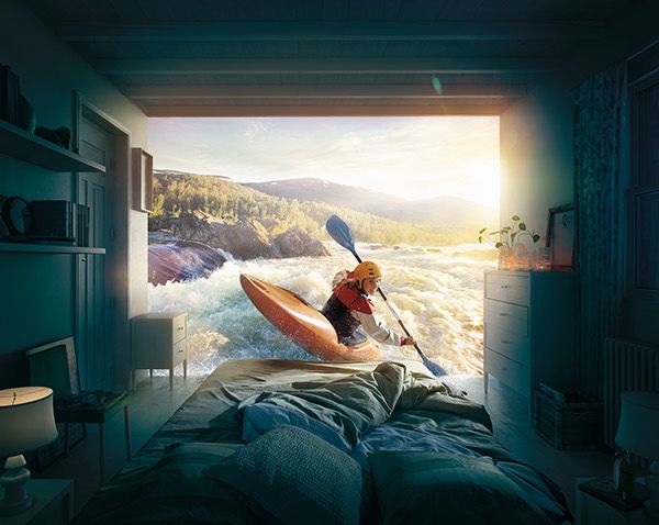 a person in a room with a bed and a kayak on the water at sunset