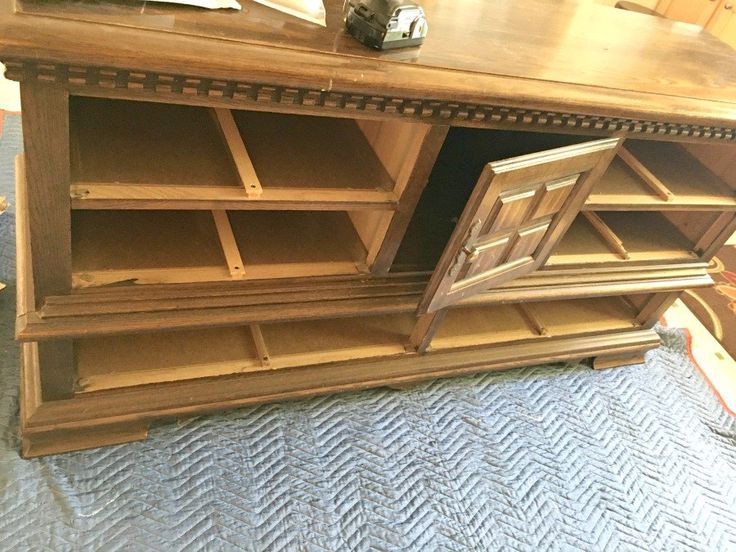 a large wooden bookcase with open doors on the front and bottom shelves, sitting on top of a blue carpeted floor