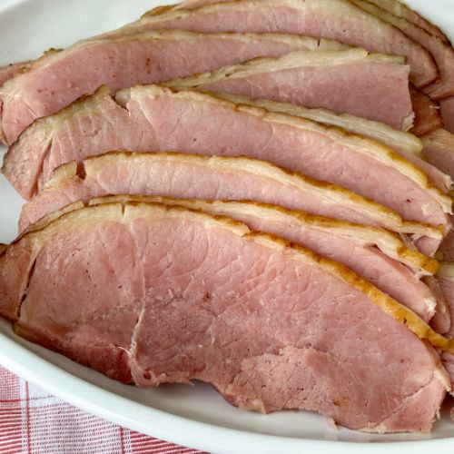 sliced ham on a white plate with red and white checkered table cloth