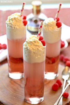 three glasses filled with ice cream and raspberries on top of a wooden tray