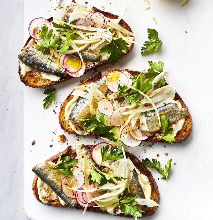 three pieces of bread with fish, radishes and onions on them sitting on a white surface