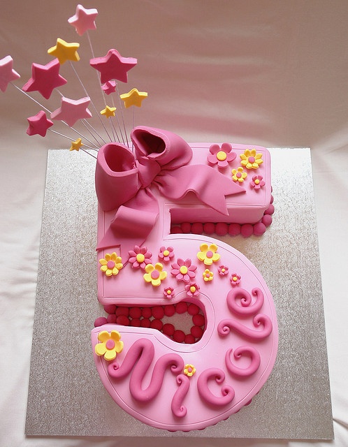 a pink birthday cake with flowers and stars on the number five, decorated in fondant