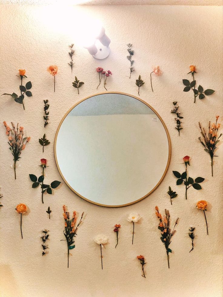 a mirror that has some flowers on the wall in front of it and a light above it