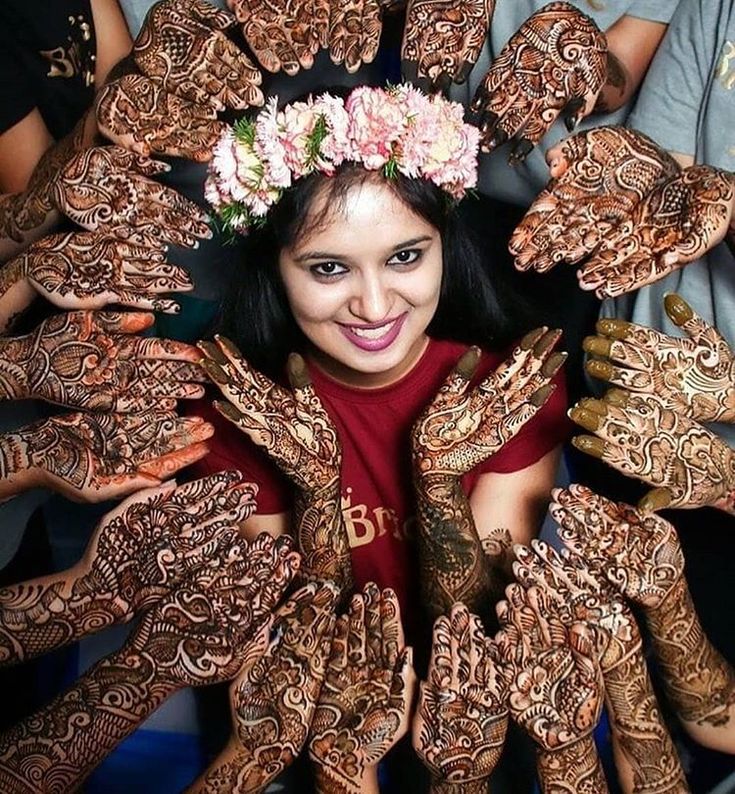 a woman with henna on her face surrounded by hands and flowers in her hair