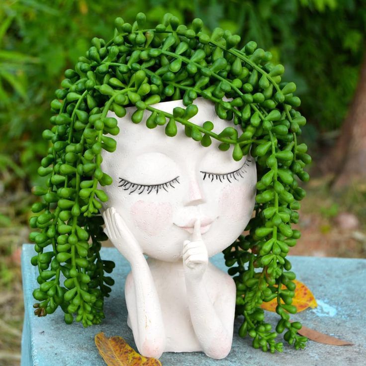 a white statue sitting on top of a blue table covered in green leaves and plants