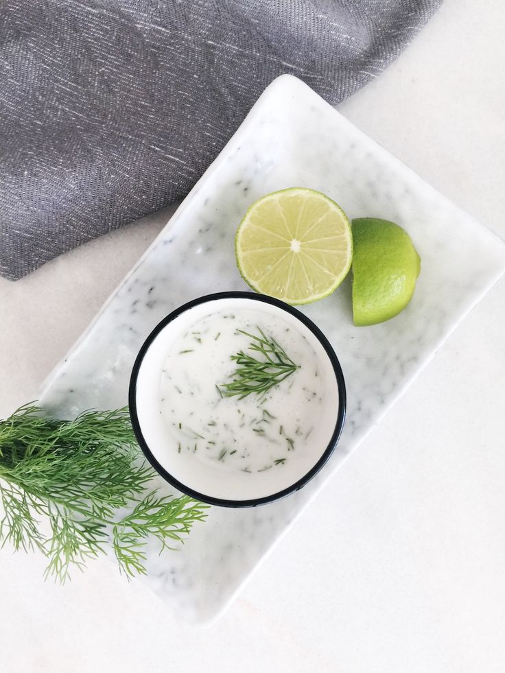 a white plate topped with a bowl of yogurt next to two limes