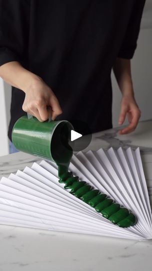 a person pouring green liquid on top of a white fan with paper folded around it