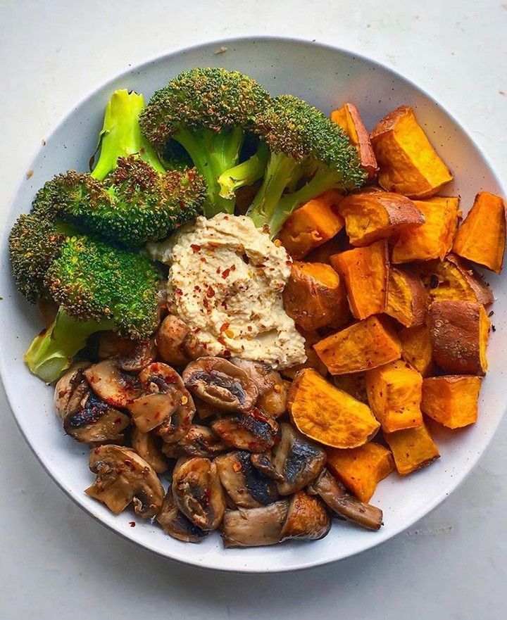 a white plate topped with broccoli, sweet potatoes and other food items on top of a table