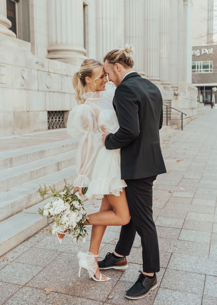 a bride and groom walking down the street in front of an old building with columns