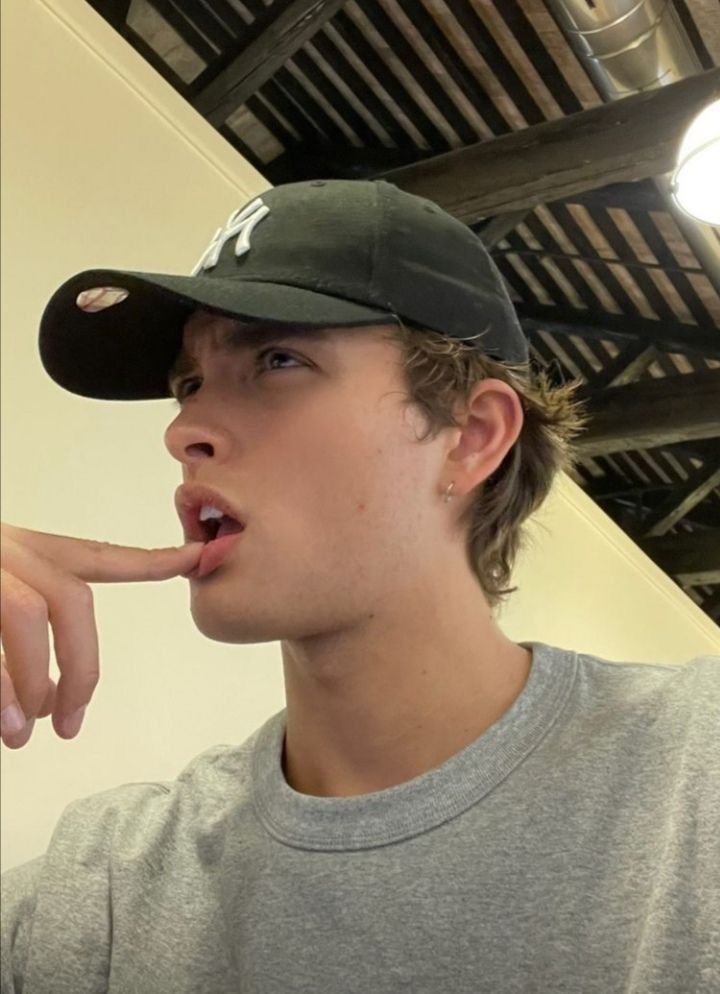 a young man wearing a baseball cap is making a funny face while holding his finger to his mouth