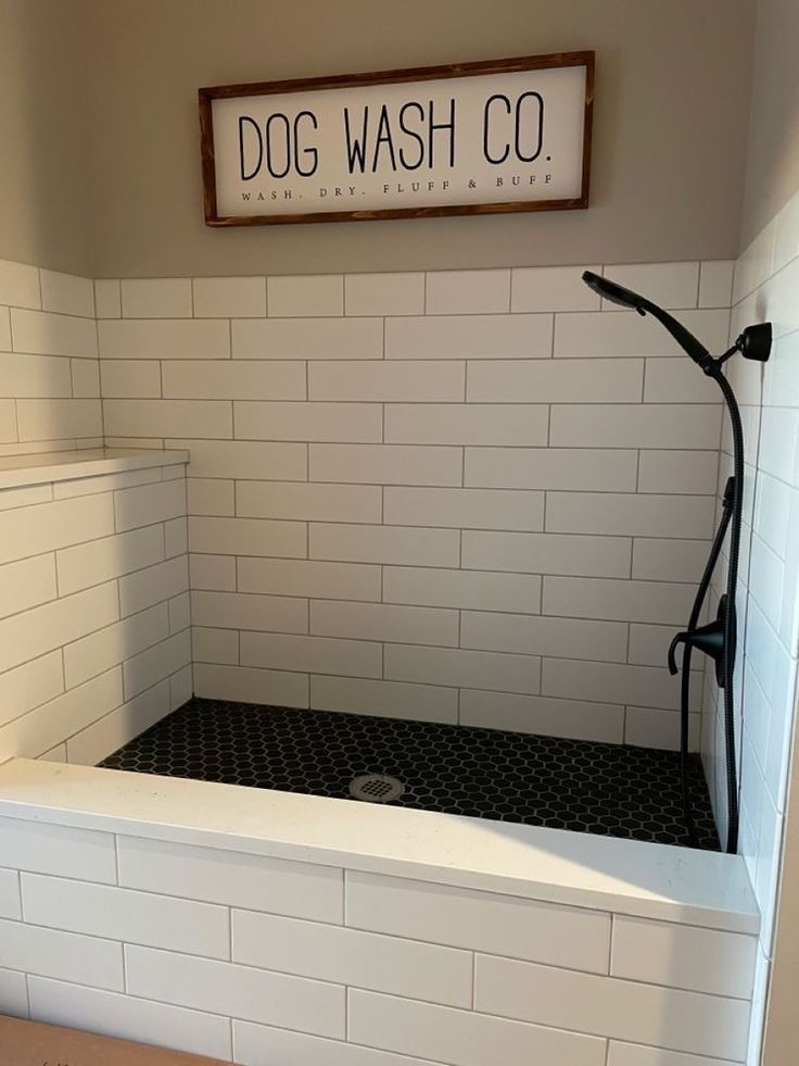 a white tiled bathroom with a dog wash co sign above the bathtub and shower head