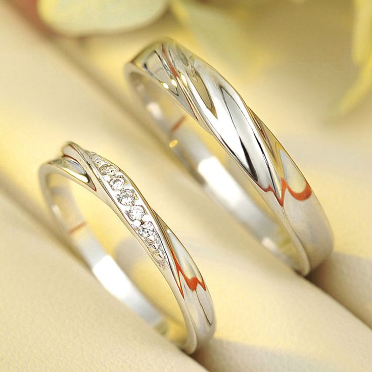 two wedding rings sitting next to each other on top of a white surface with flowers in the background