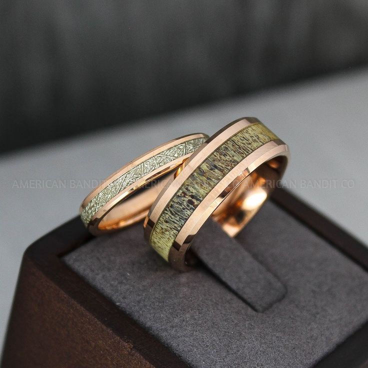 two wedding bands with gold and green wood inlays are sitting on top of a box