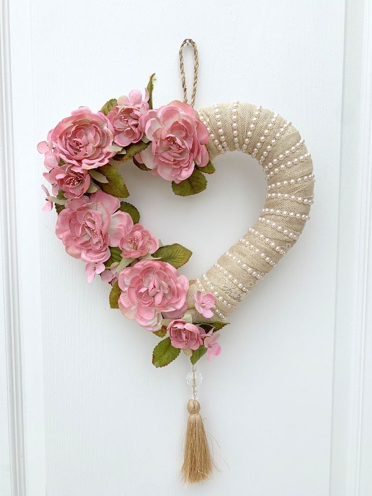 a heart shaped wreath with pink flowers hanging from it