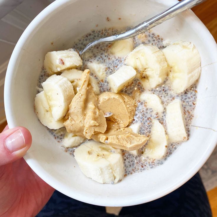 a person holding a bowl of oatmeal with bananas and peanut butter in it