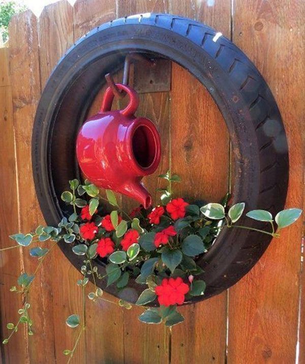 a red watering can hanging from a tire with flowers in the center and green leaves around it