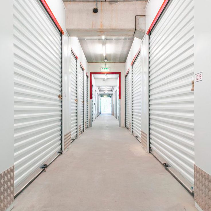 a long hallway with white and red doors leading to the exit way for storage units