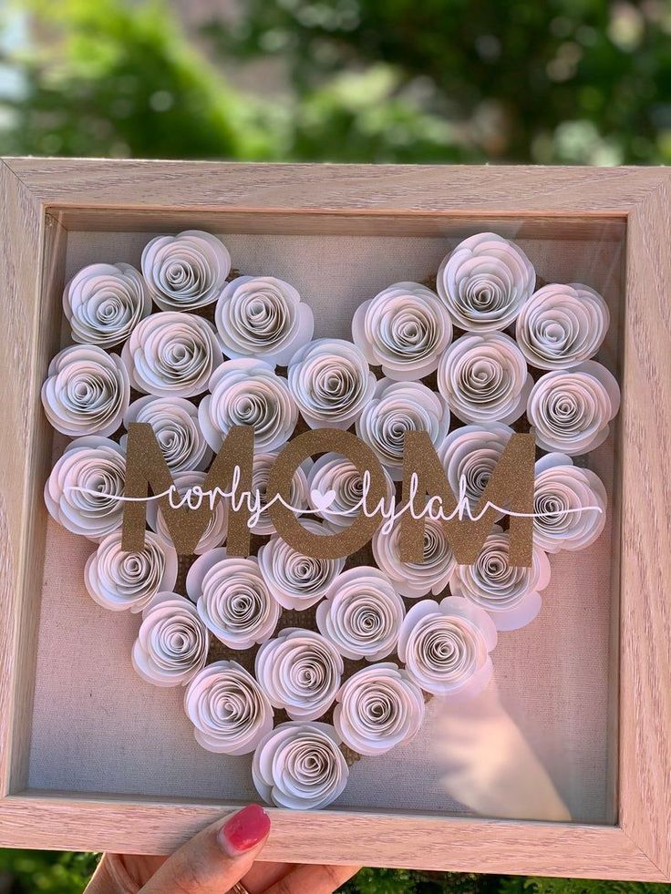 a person holding up a shadow box with rolled paper flowers in the shape of a heart