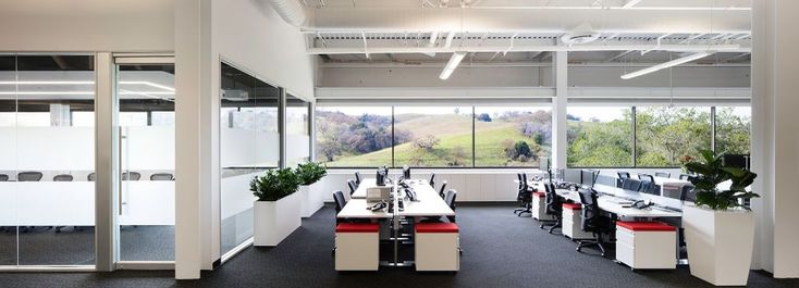 an empty office with desks and chairs in front of large windows overlooking the valley