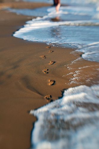 a person walking along the beach with footprints in the sand and waves crashing on them