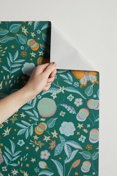 a person's hand on top of a green floral wallpaper with white envelope