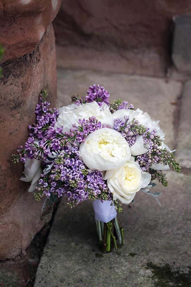 a bouquet of white and purple flowers sitting on top of a cement slab next to a brick wall