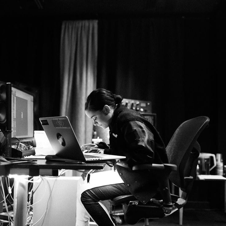 a woman sitting at a desk with a laptop computer in front of her, while looking at the screen