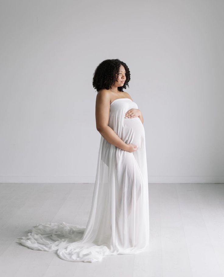 a pregnant woman wearing a white gown and standing in the middle of an empty room